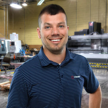 Corporate headshot of business owner in blue shirt, manufacturing background
