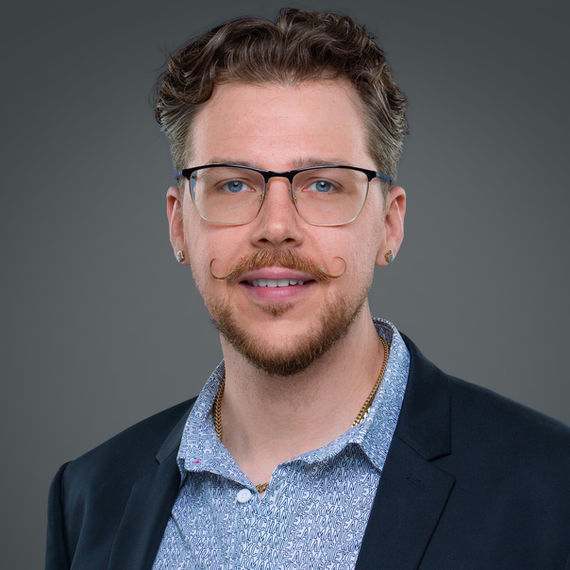 Professional headshot of a man wearing glasses and a dark jacket.