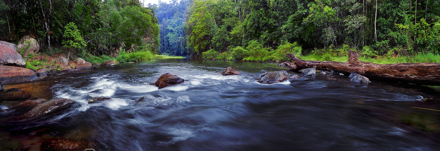 An aerial landscape photograph captured by a drone in the middle of the mountain creek with green tropical forest in the background