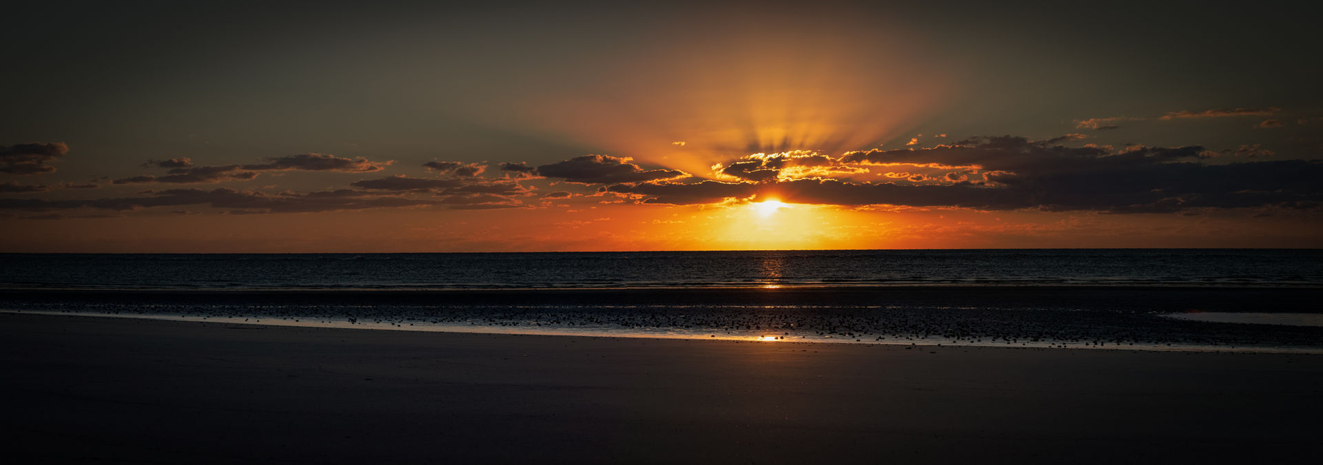 A photo of the spectacular seaside sunset with sunbeams breaking through the clouds.