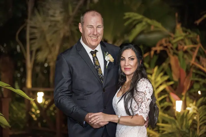 The bride and groom smile together among tropical foliage and warm evening lights after the reception begins in Cairns 