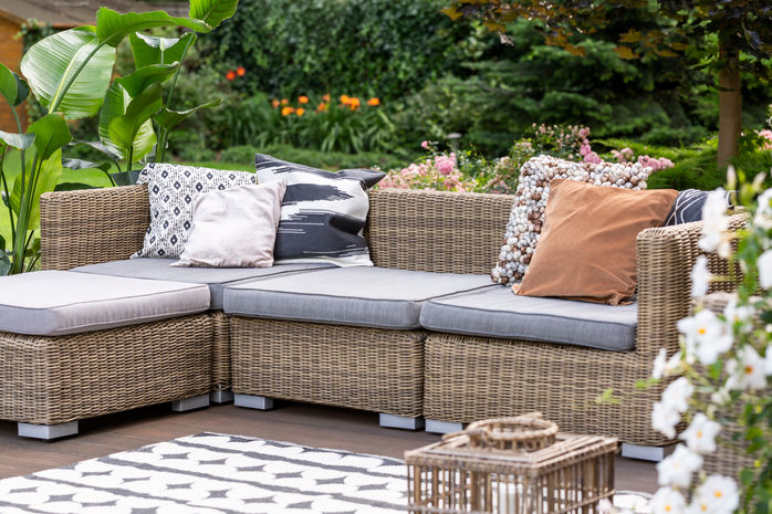 Outdoor patio highlighting trendy Australian pale brown wicker furniture creates an atmosphere of connection between nature and suburban living. Neutral and earthy tones are utilised and a background of flowers and vegetation surrounds the outdoor patio in Tropical North Queensland. Real estate photography, Cairns, Queensland, Australia.