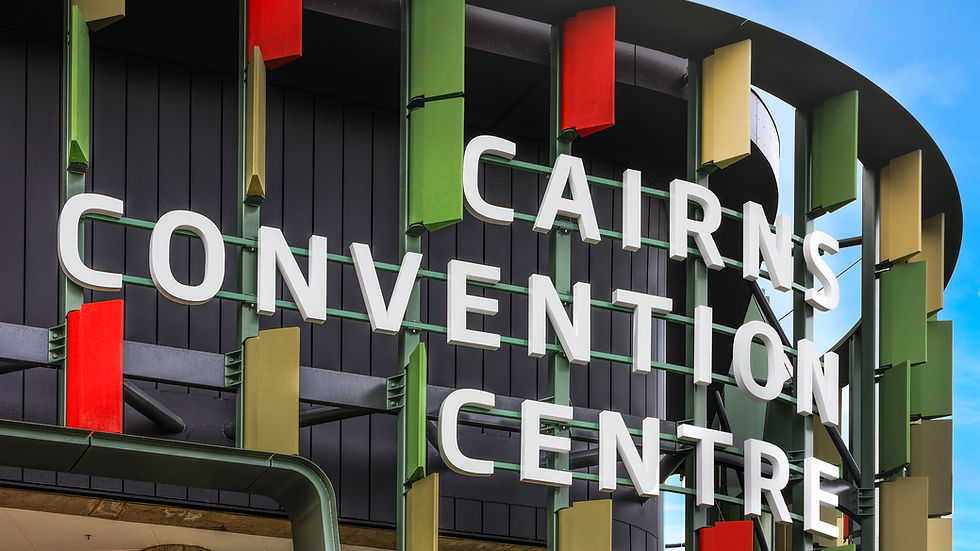 Sign of Cairns Convention Centre with bold white letters against a dark background. Green, red, and yellow accents, blue sky visible.