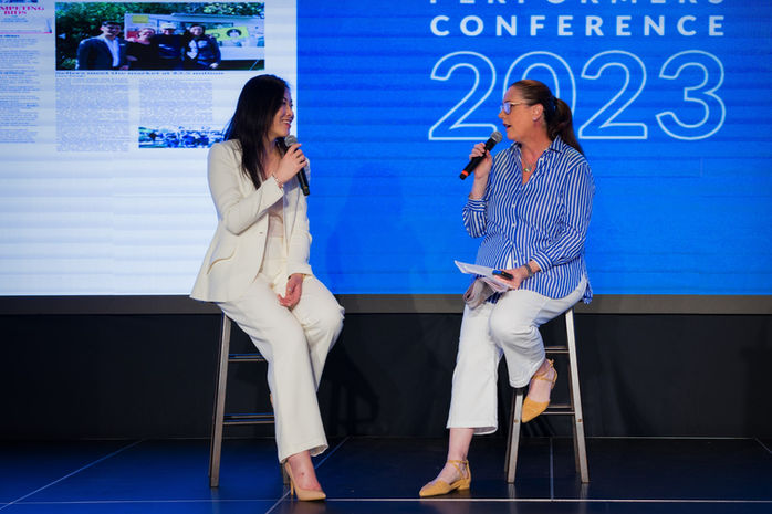 Two female conference speakers seated on stage in conversation.