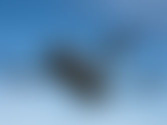 Drone from iDrone Pro Cairns flying in clear blue sky, four propellers spinning. The drone is gray with visible lenses and "Mavic 4 Pro" text on its arm.