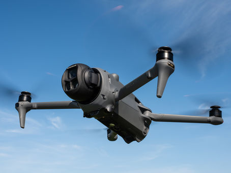 Drone from iDrone Pro Cairns flying in clear blue sky, four propellers spinning. The drone is gray with visible lenses and "Mavic 4 Pro" text on its arm.
