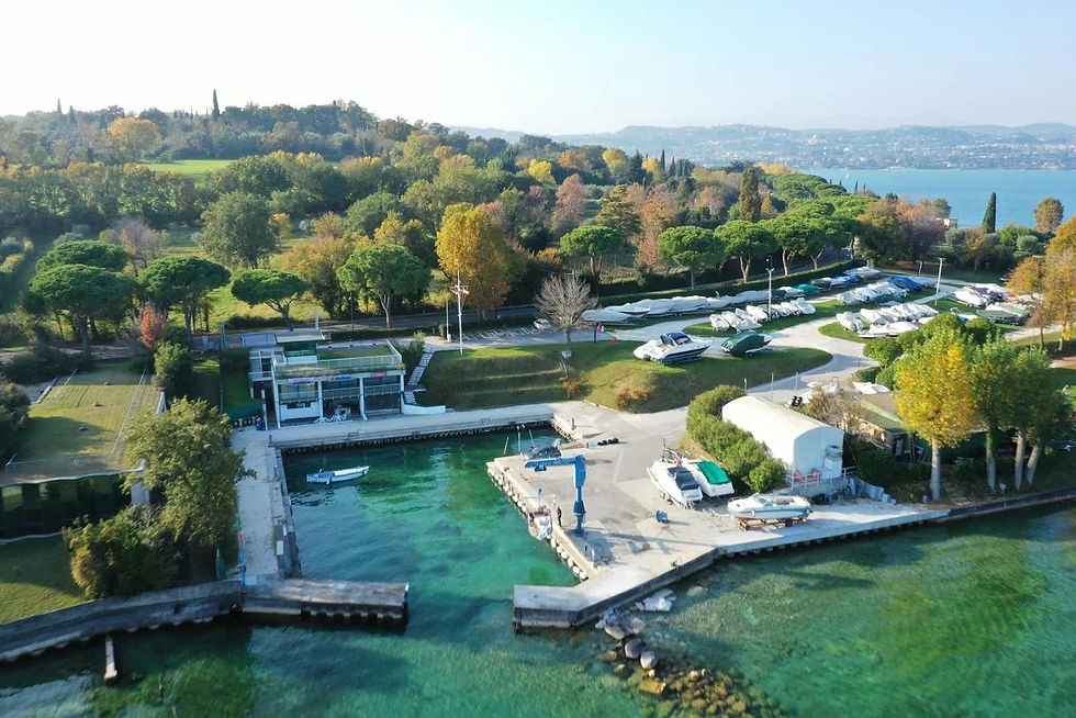 Aerial view of a marina with boats on green water, lush trees, and parked boats in the background. The setting is serene and vibrant.