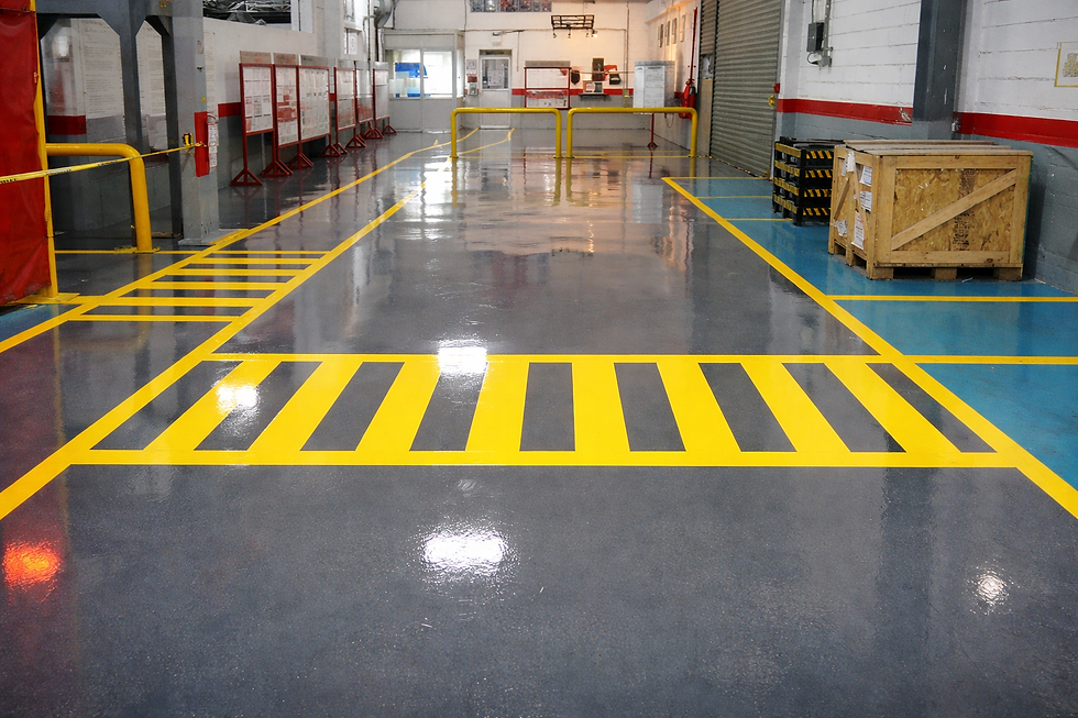 Piso industrial epóxico con señalización de seguridad amarilla y negra, áreas delimitadas y superficie brillante en planta.