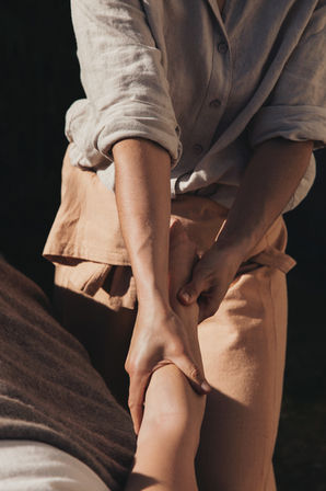 Close up image of a softly lit scene showing a therapist’s gentle hands massaging clients arm. The natural light highlights the warmth and tranquility of the moment, emphasizing themes of relaxation, healing, and human connection.