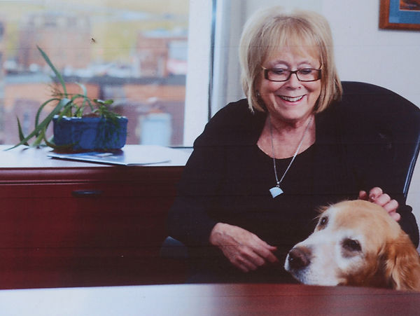 Dulcie McCallum with her dog at her desk. A plant sits on the desk and a window beyond it.