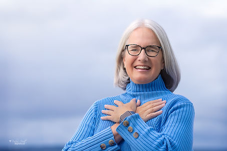 A photo of Karen J Williams crossing her arms over her heart and smiling at the beach