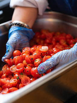 Hands in blue gloves mixing fresh halved cherry tomatoes in a tray.