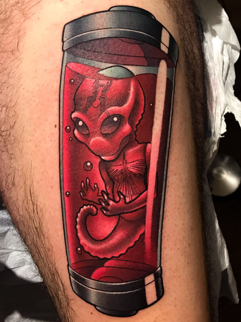 New school color tattoo on a thigh of an alien fetus surrounded by red liquid in a tube by top Connecticut tattoo artist Cracker Joe
