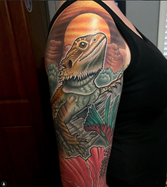 The top portion of a larger color tattoo sleeve on a woman featuring a lizard and flowers