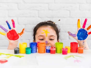 girl-looking-multicolored-paint-bottles-white-desk-with-her-painted-palms.jpg