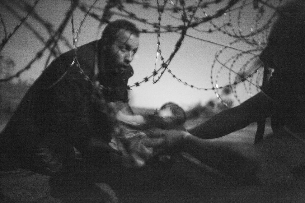 Un hombre pasa un bebé por debajo de la alambrada entre Serbia y Hungría en Röszke, Hungría, 28 de agosto de 2015 © Warren Richardson, Australia