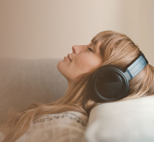 A woman reclines peacefully with headphones, eyes closed in Luma self-hypnosis practice and experiencing inner healing, self-restoration, and spiritual stillness.