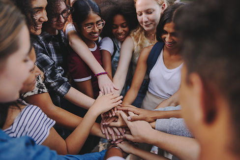 A diverse group of young people join hands in a powerful gesture of unity, teamwork, and shared purpose. Their smiles and connection radiate inclusion, community, and hope for the future.