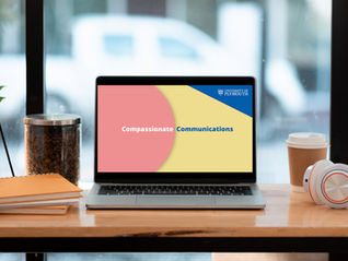 A laptop on a desk displaying a still frame from a 'Compassionate Communications' video resource