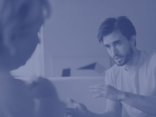 An image of a male student talking to a female member of staff in a higher education setting - perhaps a 1:1 tutorial or supervision meeting.