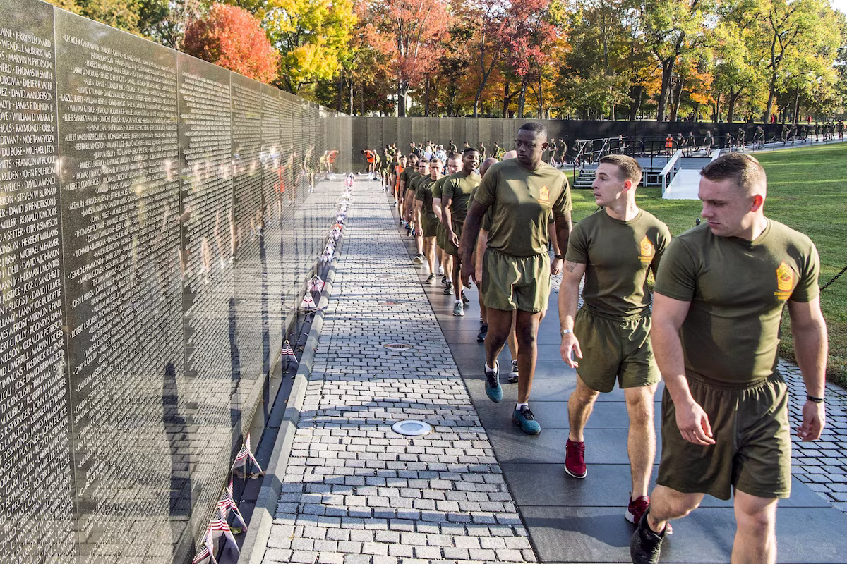 Wide shot showing veterans looking at the Vietnam Veterans Memorial, with light reflecting off the engraving of the memorial artwork.