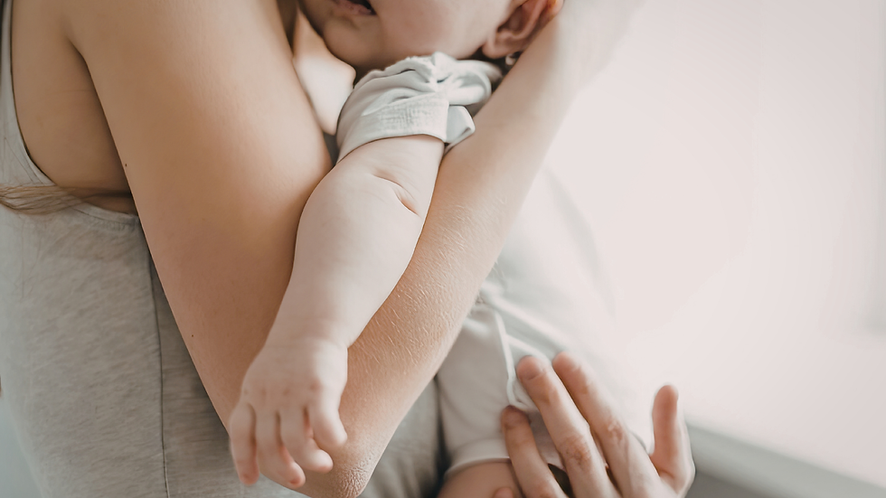 Close-up of a baby cradled in an adult's arms, wearing light clothing. Soft lighting creates a peaceful, tender mood with minimal background.