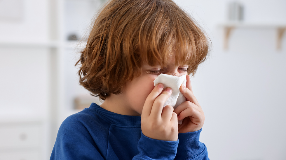 Child with brown hair in a blue sweater sneezing into a tissue