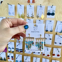 A woman's hand holds a pair of Grecian-style earrings made of jasper beads