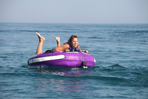 Une jeune fille est à plat ventre sur une bouée tractée par un bateau dans l'eau, elle s'amuse.