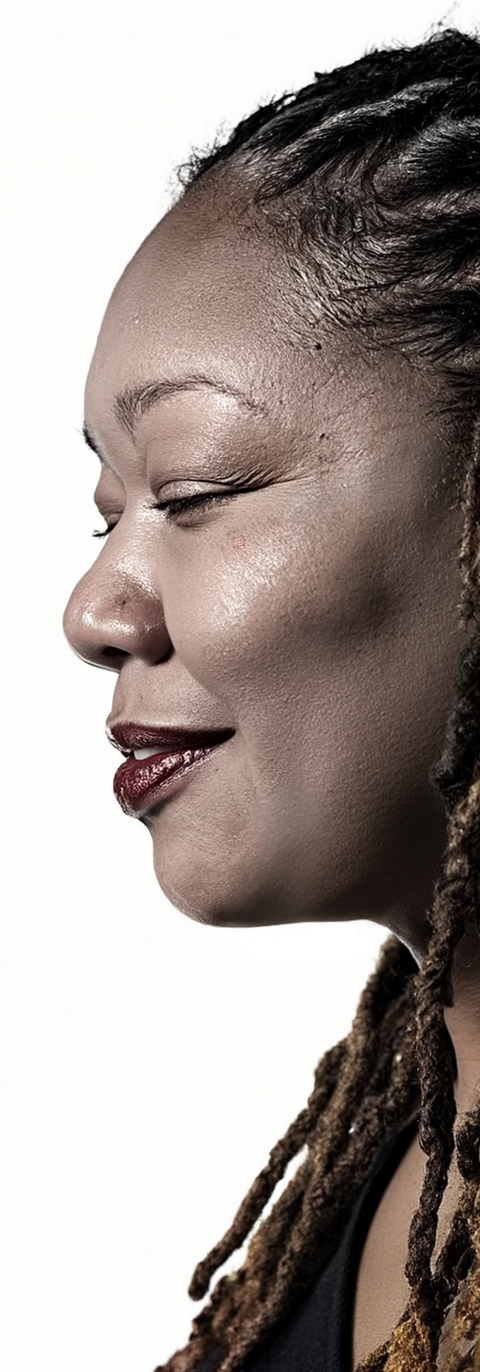 Profile headshot of K. Heshima White, an African American woman with long locs, wearing earrings and red lipstick, smiling softly with eyes closed.