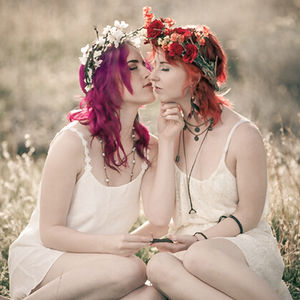 two women wearing flower crowns kissing in a field
