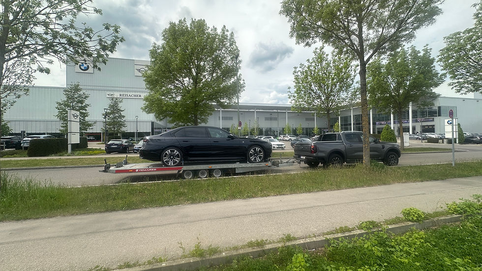 Zwarte BMW i7 xDrive60 op transportwagen, ingevoerd vanuit Duitsland via SoHo Automotive, BMW dealer op achtergrond