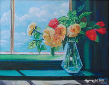 A crystal blue flower vase holding red and yellow flowers sits on a green window sill.