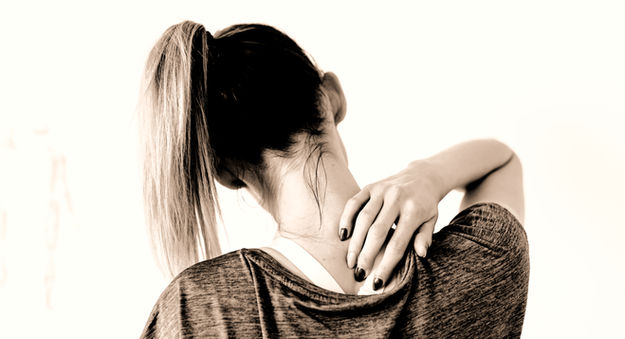 Woman from behind rubbing her painful neck and upper shoulder.