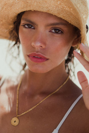 Woman wearing straw hat and gold coin necklace in Tulum