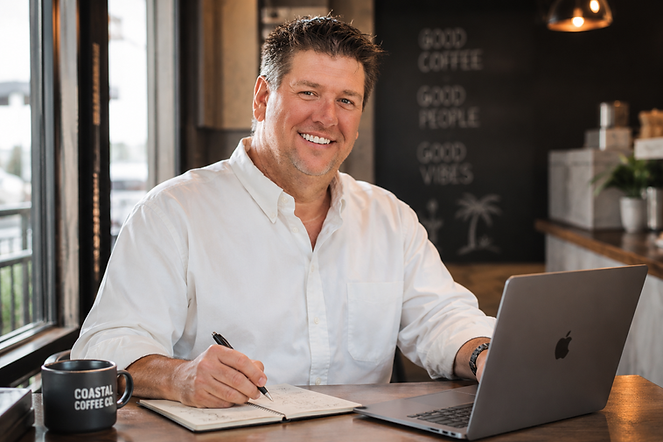 David Arnold, founder of David Arnold Creative, working on marketing strategy and customer acquisition planning at a coffee shop with a laptop and notebook.