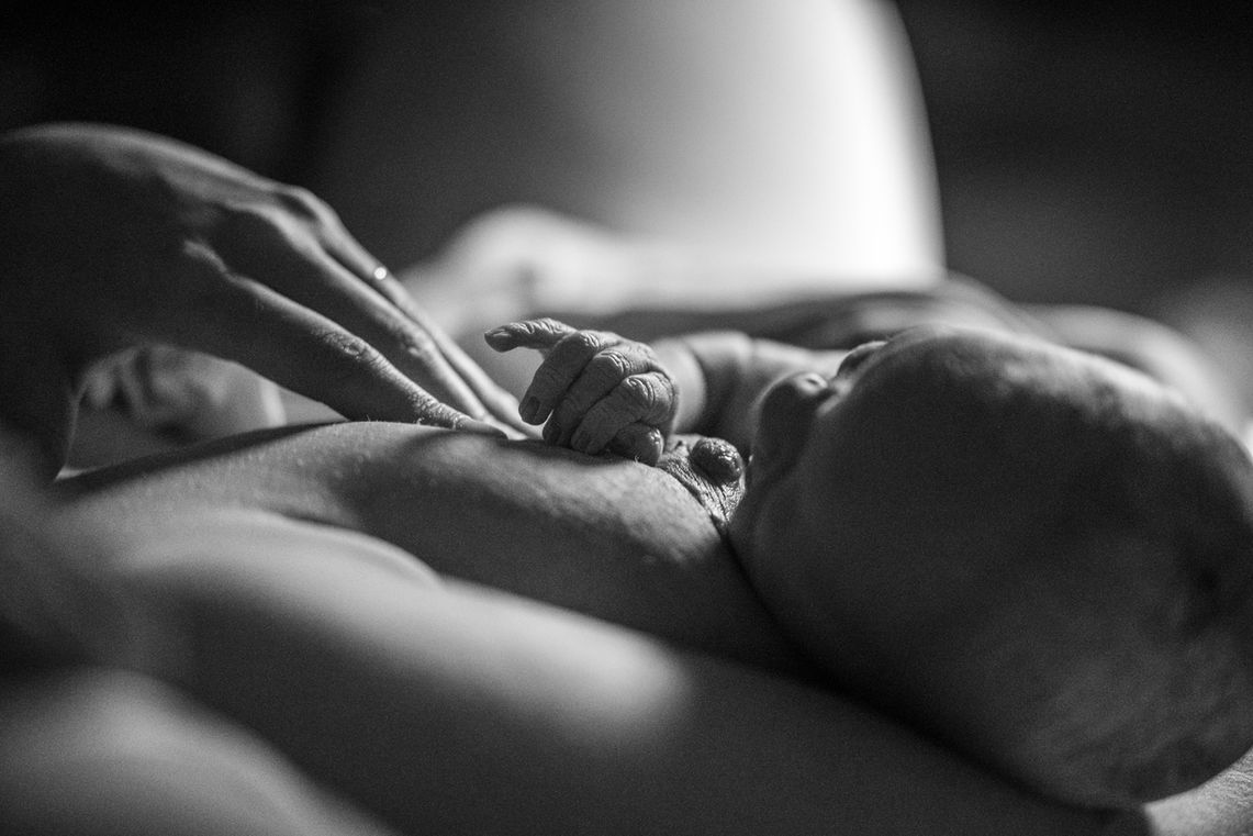 Detailfoto van mamahand die baby probeert te helpen om tepel te vinden bij eerste borstvoeding