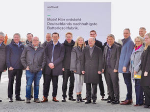 Gruppenfoto vor dem Northvolt-Bauschild mit Olaf Scholz, Robert Habeck, Daniel Günther, Claus Ruhe Madsen, Peter Carlsson, Christopher Haux und weiteren Beteiligten am Baubeginn in Heide. Bürgermeister Oliver Schmidt-Gutzat steht als Fünfter von rechts im mittelblauen Sakko.