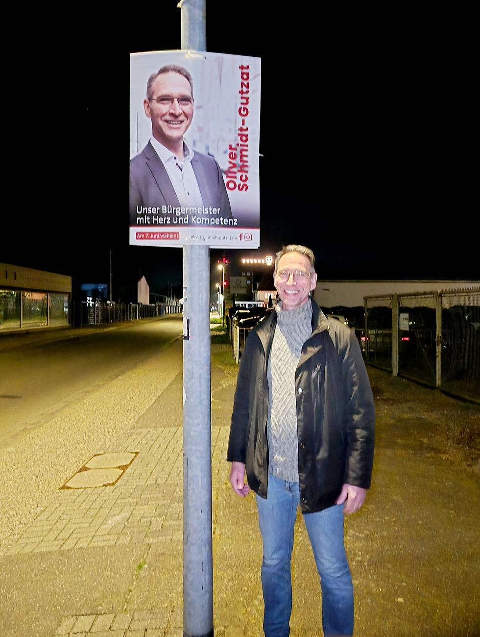 Wahlplakat von Oliver Schmidt-Gutzat an einer Straßenlaterne bei Nacht, er steht daneben
