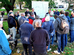 Oliver Schmidt-Gutzat und mehrere Personen stehen im Freien vor einem Lageplan und hören einer Erläuterung zur Verkehrsführung zu.