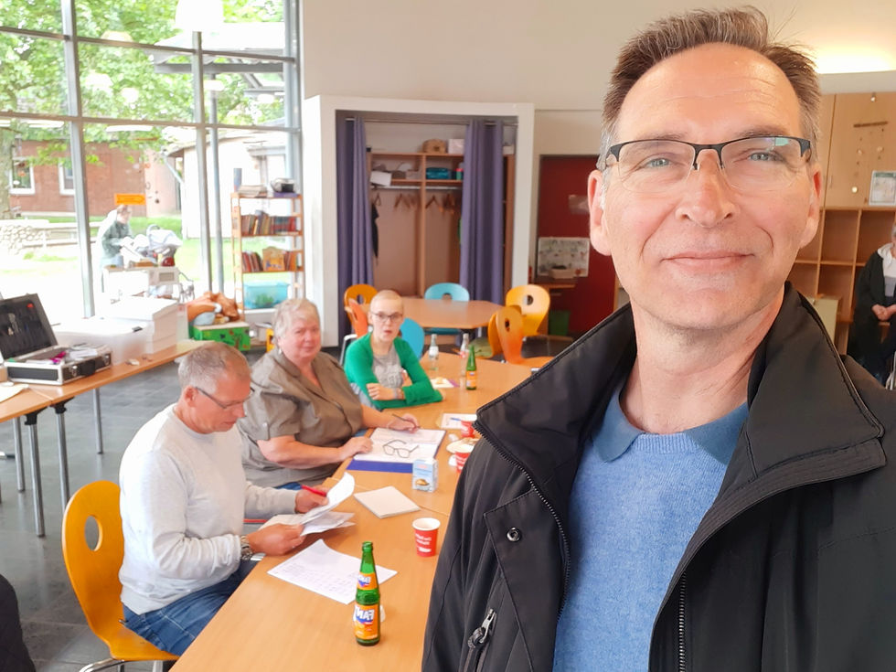 Besuch im Wahllokal Klaus-Groth-Schule in Heide, Wahlhelferinnen und Wahlhelfer sitzen an Tischen, Oliver Schmidt-Gutzat im Vordergrund.