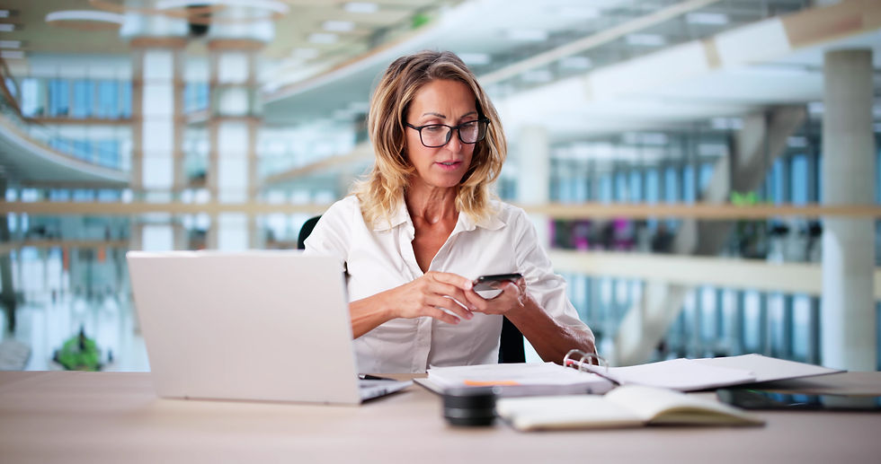 Mitarbeiterin prüft Eingangsrechnung mit Laptop und Smartphone am Schreibtisch