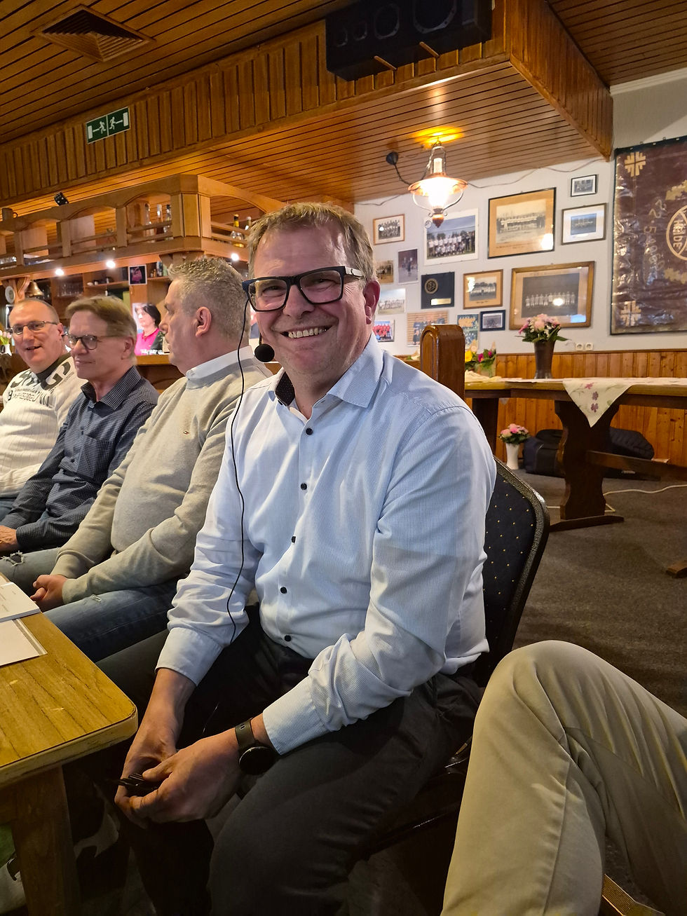 Dirk Löbkens mit Headset bei der Mitgliederversammlung des MTV Heide, weitere Personen sitzen neben ihm