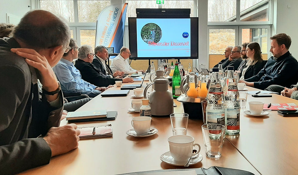 Teilnehmende des Arbeitskreises Dithmarscher Wasserwelt bei einer Sitzung mit Getränken und Unterlagen. Auf einem Bildschirm ist das Logo des Projekts zu sehen.