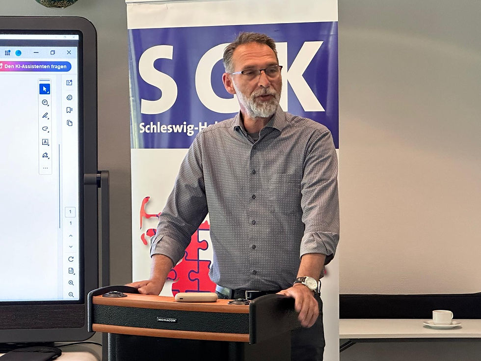 Oliver Schmidt-Gutzat begrüßt die Teilnehmenden der SGK-SH-Mitgliederversammlung am Rednerpult, SGK-Banner im Hintergrund.