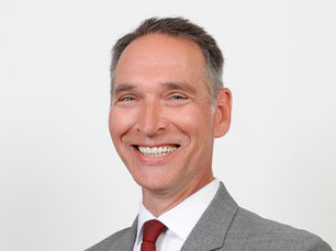 Porträt von Oliver Schmidt-Gutzat im grauen Anzug und roter Krawatte, offizielles Bewerbungsfoto für die Bürgermeisterwahl 2026 in Heide.