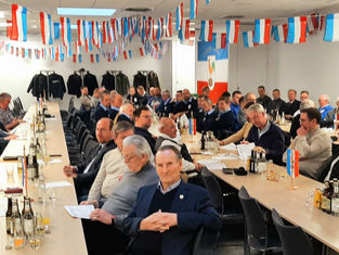 Generalversammlung der Österegge: Rund 90 Personen sitzen an Tischen in einem festlich geschmückten Raum. An den Wänden hängen rot-weiß-blaue Wimpel, ein Redner steht rechts am Pult.