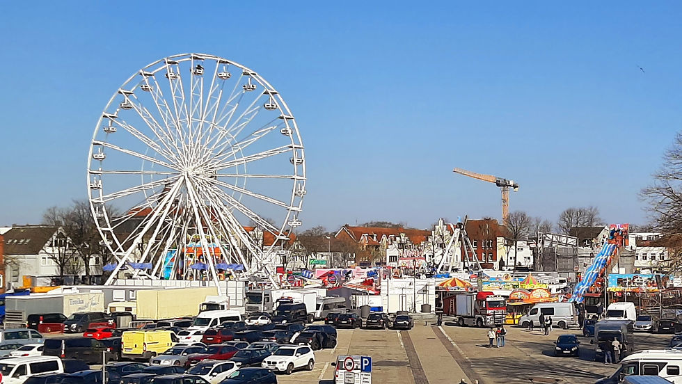 Blick auf den Heider Frühjahrsjahrmarkt auf dem größten Marktplatz Deutschlands mit Riesenrad, Fahrgeschäften und vielen Besuchern bei Tageslicht.