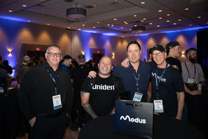 Four men smiling in Modus shirts at an event with the crowd.