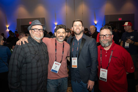Four men smiling together with name tags at an event gathering.